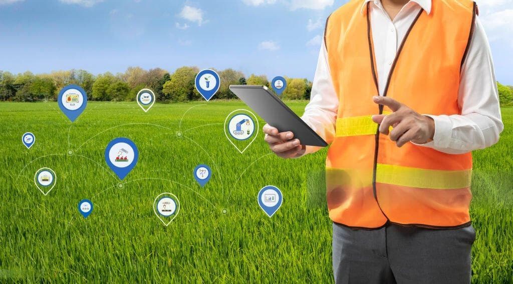 Field worker in a high-visibility vest checking a tablet in a crop field, with data overlay icons showing connected field operations