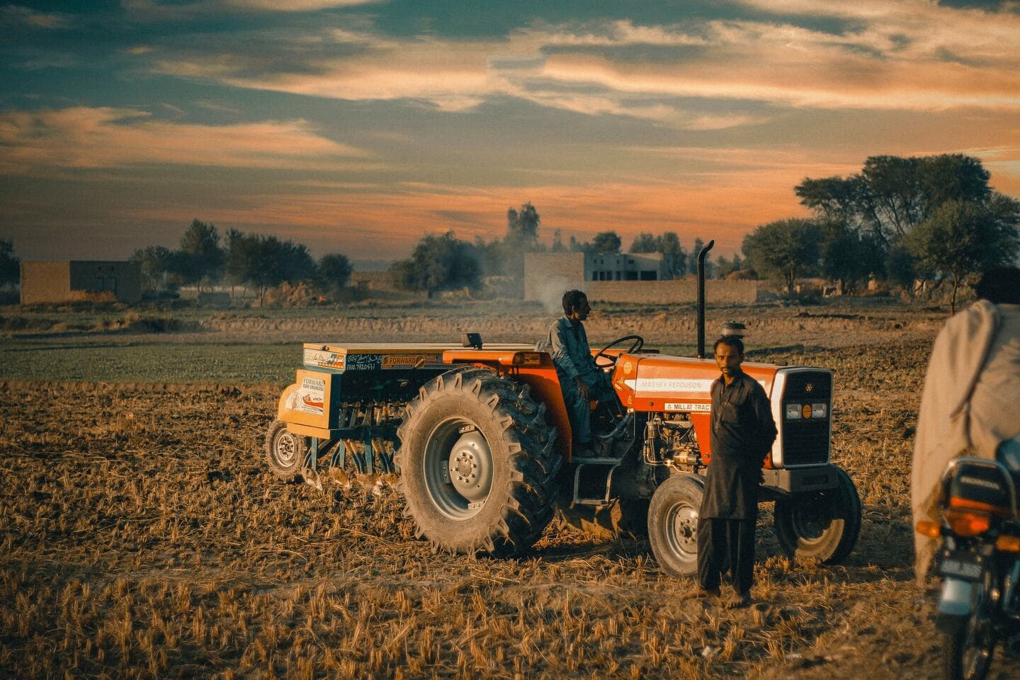 Farmers with a tractor and seeding equipment in a field at dusk, representing field-level resource monitoring