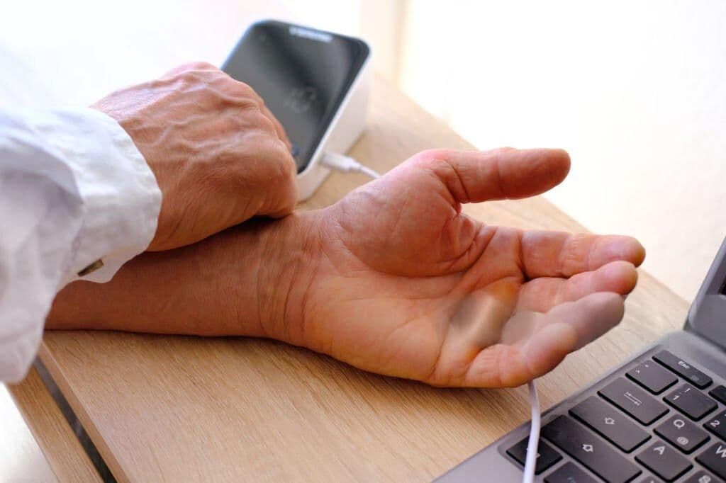 Clinician checking a patient pulse at a desk with a laptop, representing clinical data handling and compliance