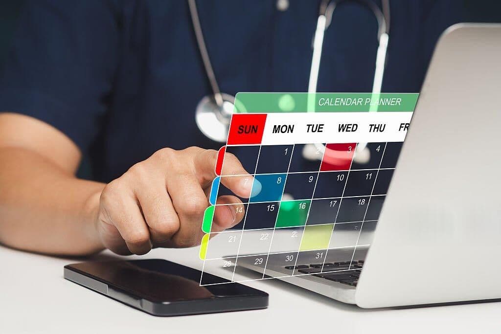 Clinician with a stethoscope tapping a calendar planner overlay above a laptop, representing appointment scheduling